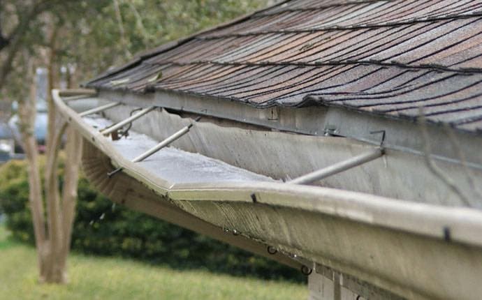 Close-up of a clogged gutter with water pooling on a sloped roof, highlighting drainage issues.