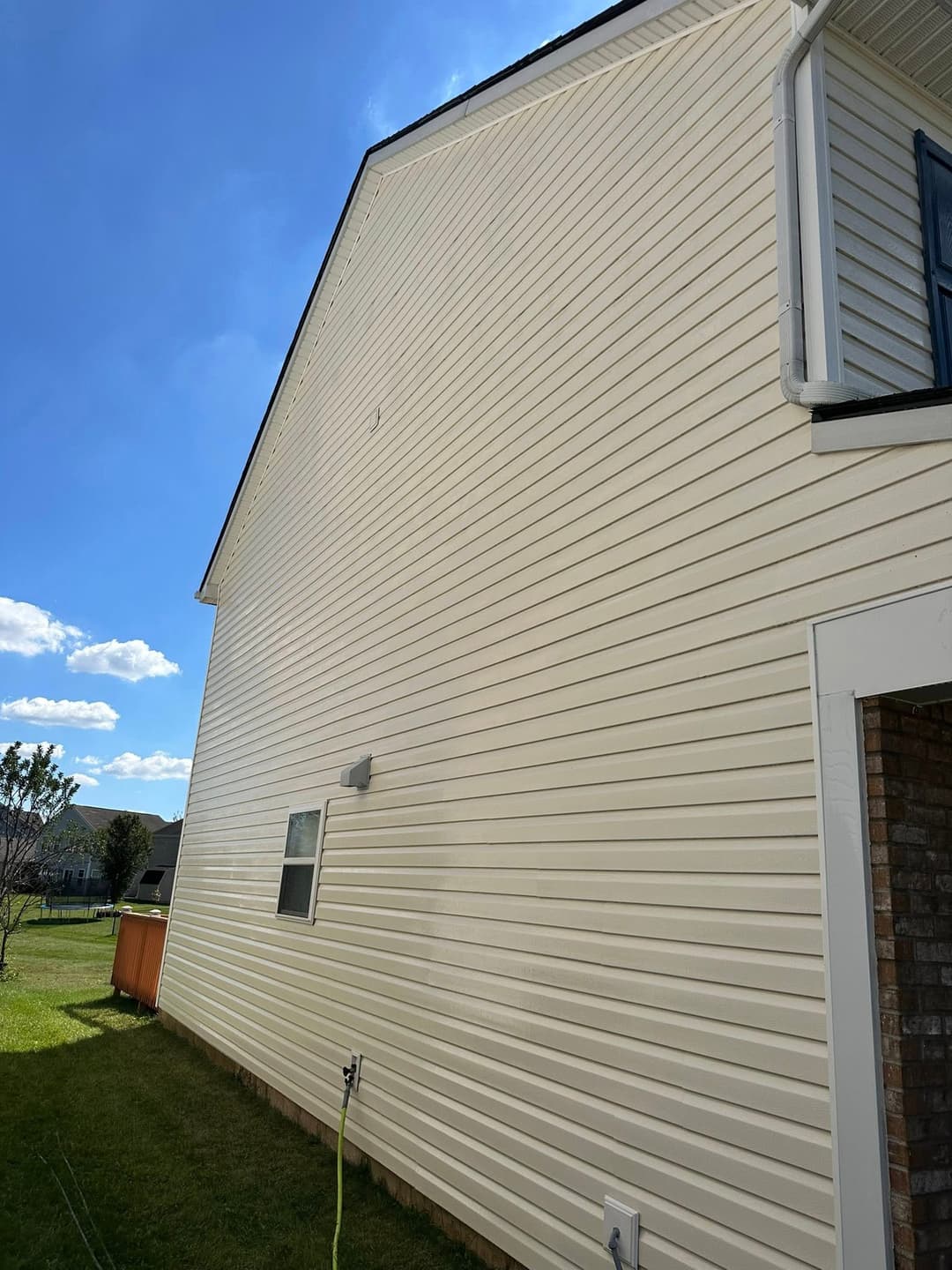 Side view of a house with vinyl siding, clear blue sky, and grassy yard.