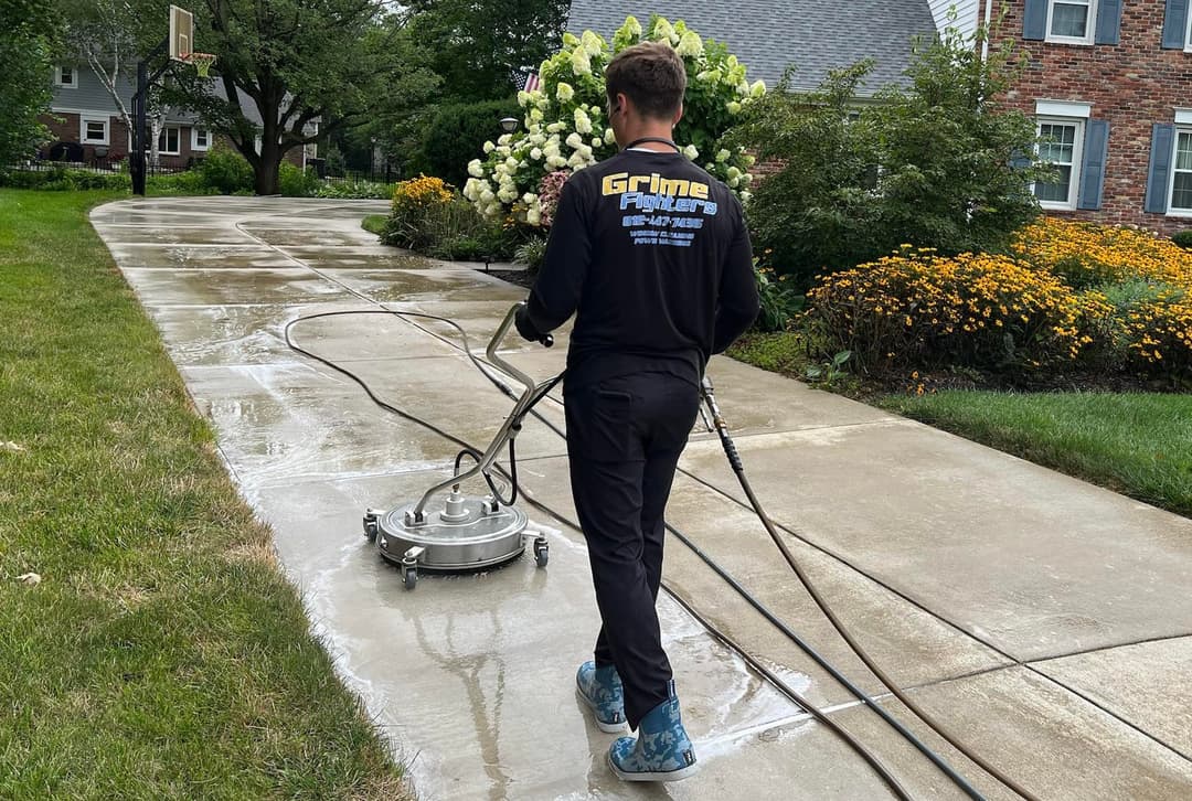 Pressure washing service cleaning a driveway, revealing a spotless surface and vibrant landscaping.