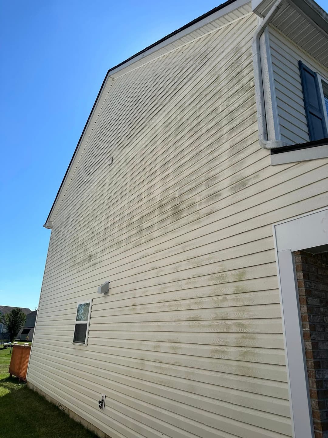 Dirty exterior of a house showing stains on vinyl siding under a clear blue sky.