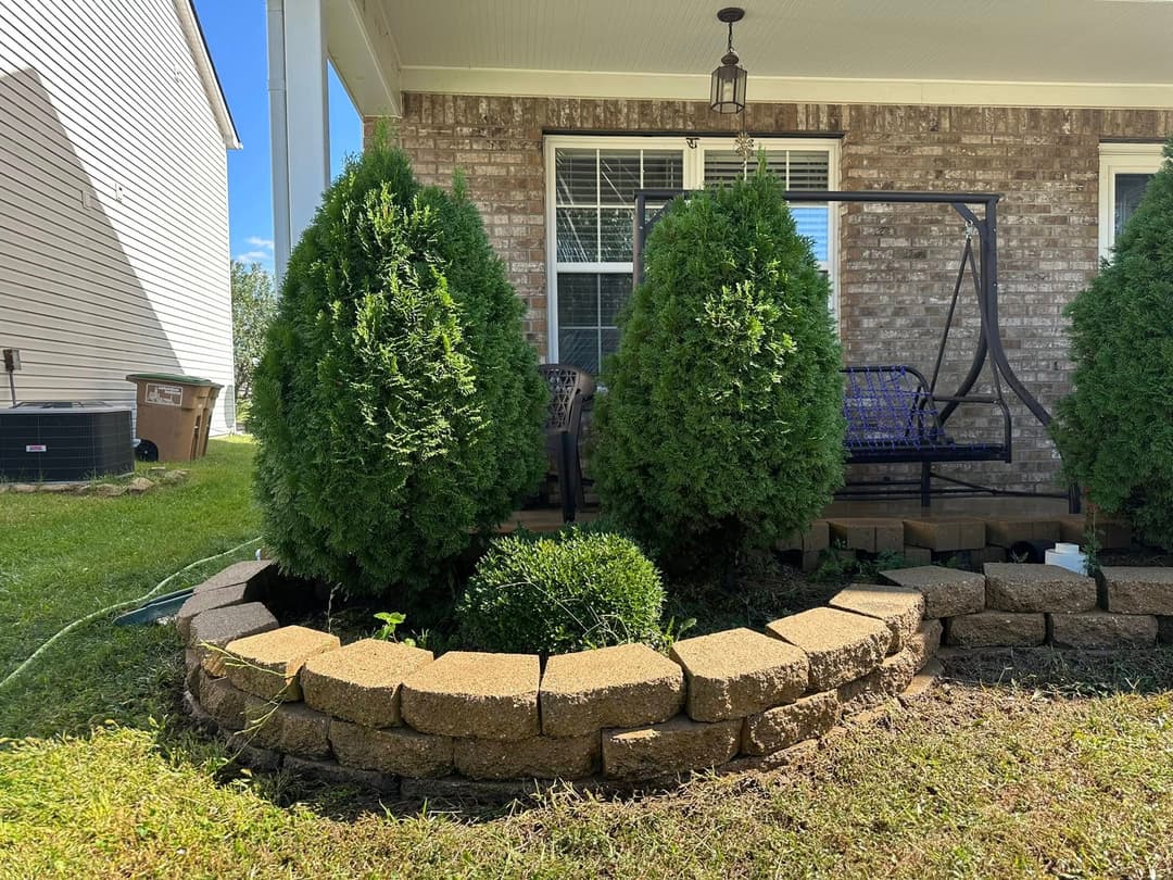 Lush green shrubs flanking a covered porch with stone landscaping in a residential yard.