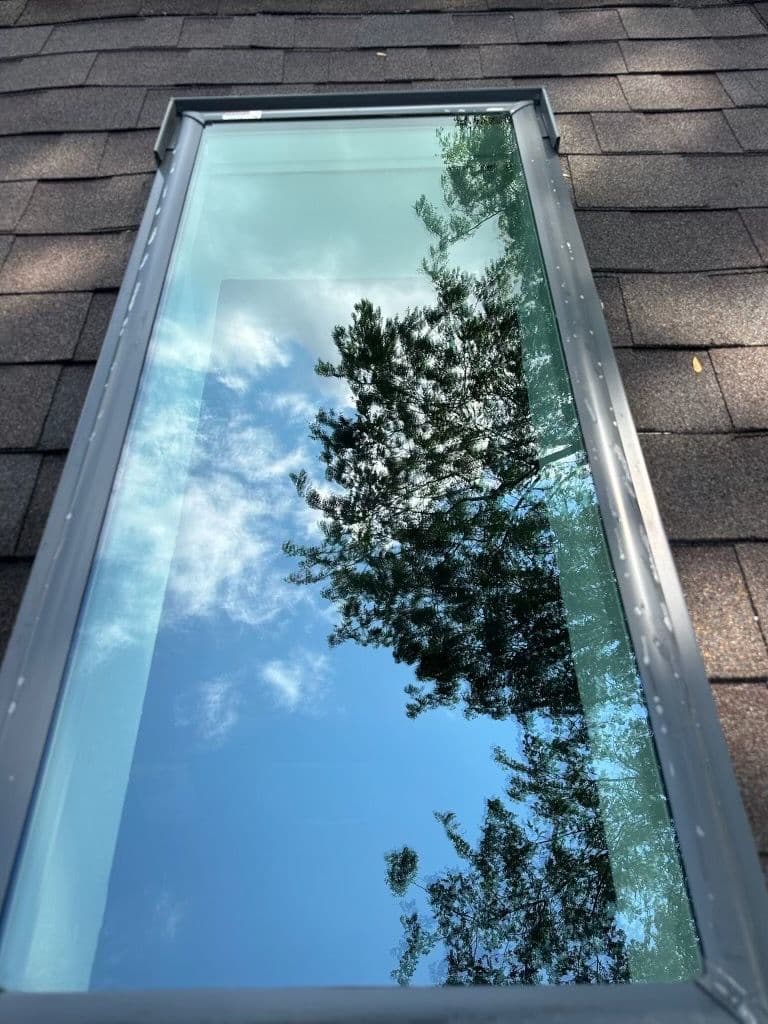 Skylight reflecting trees and sky on a shingled roof.