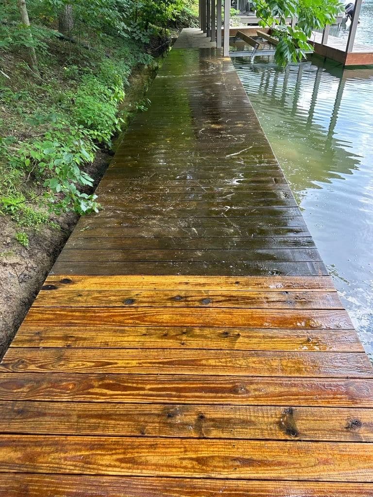 Waterfront wooden dock with newly stained planks, surrounded by lush greenery.