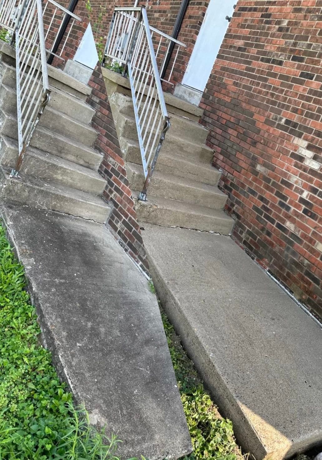 Uneven concrete steps and wheelchair ramp at a brick building entrance, highlighting accessibility issues.