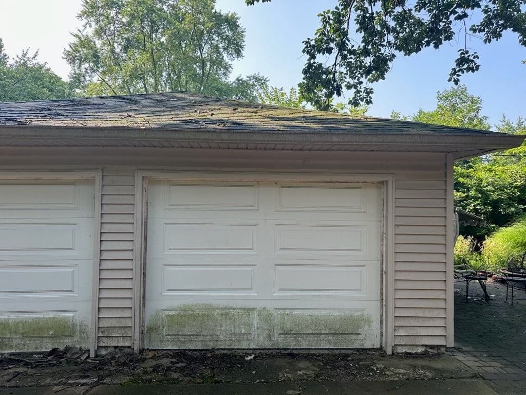 Two garage doors on a weathered building with visible mold and a lush green surroundings.