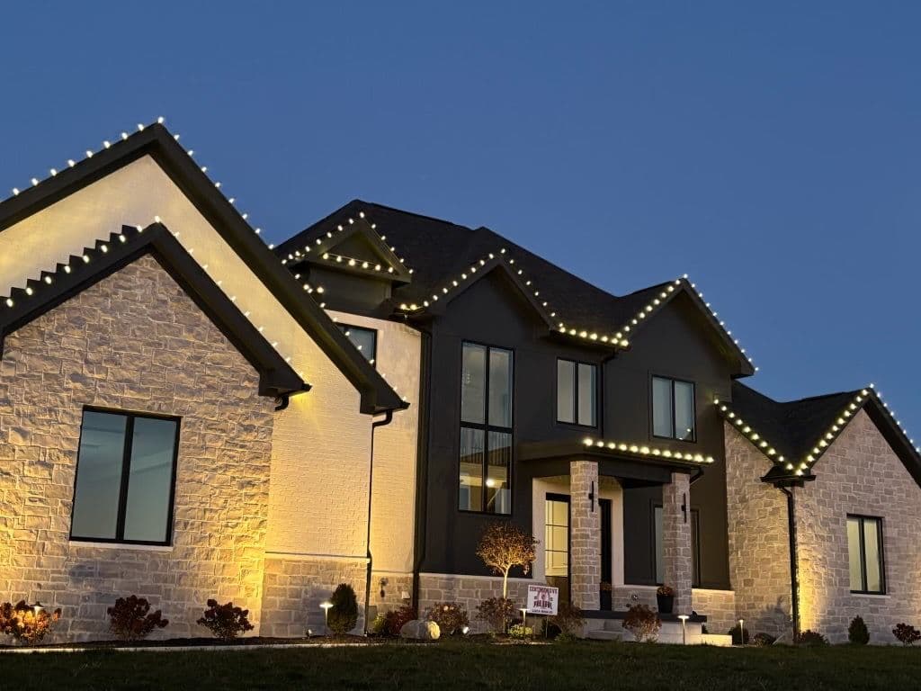Modern home adorned with decorative lights at dusk, highlighting stone and dark siding features.