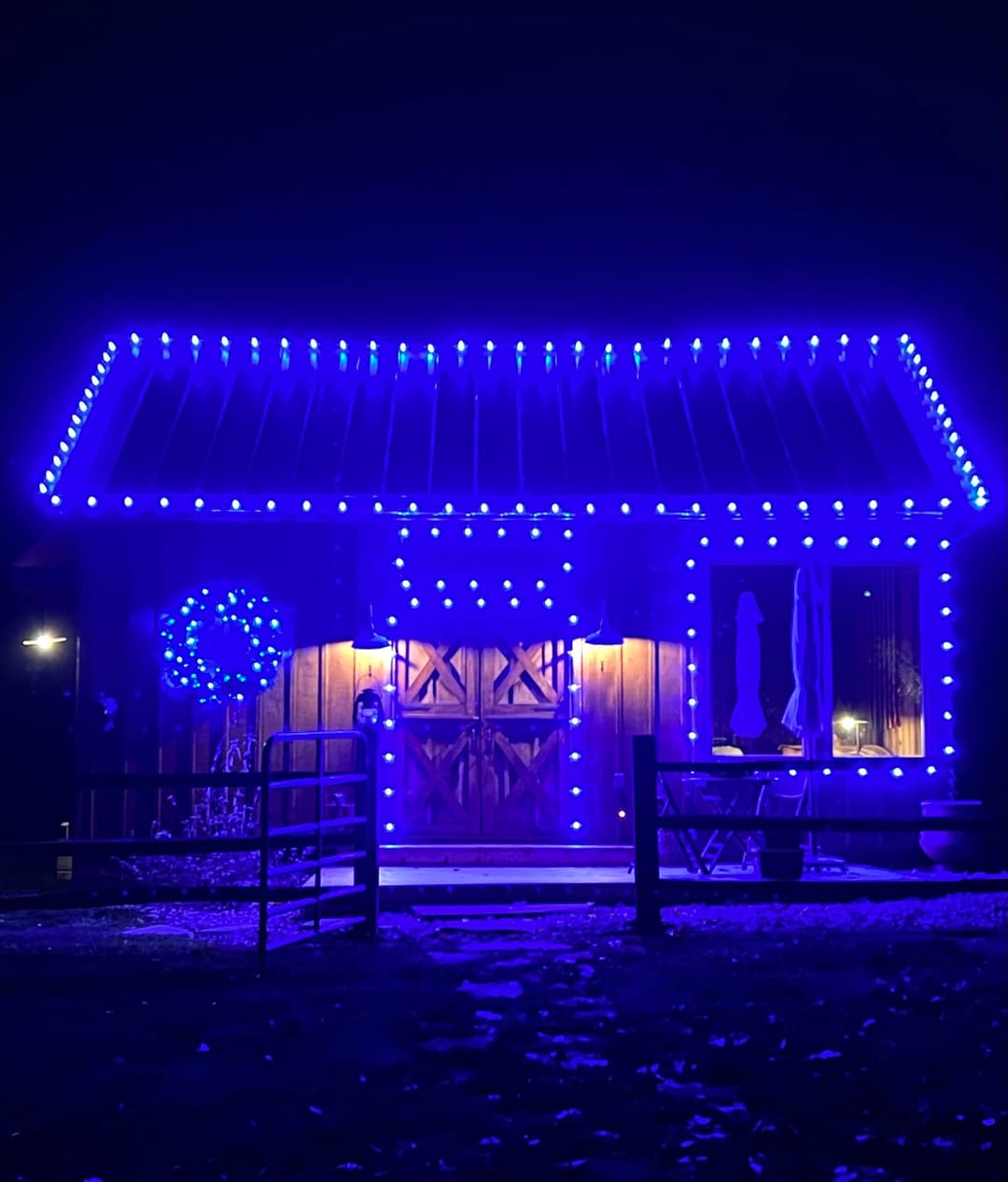 Blue-lit cabin with decorations, featuring a festive wreath and illuminated entrance at night.
