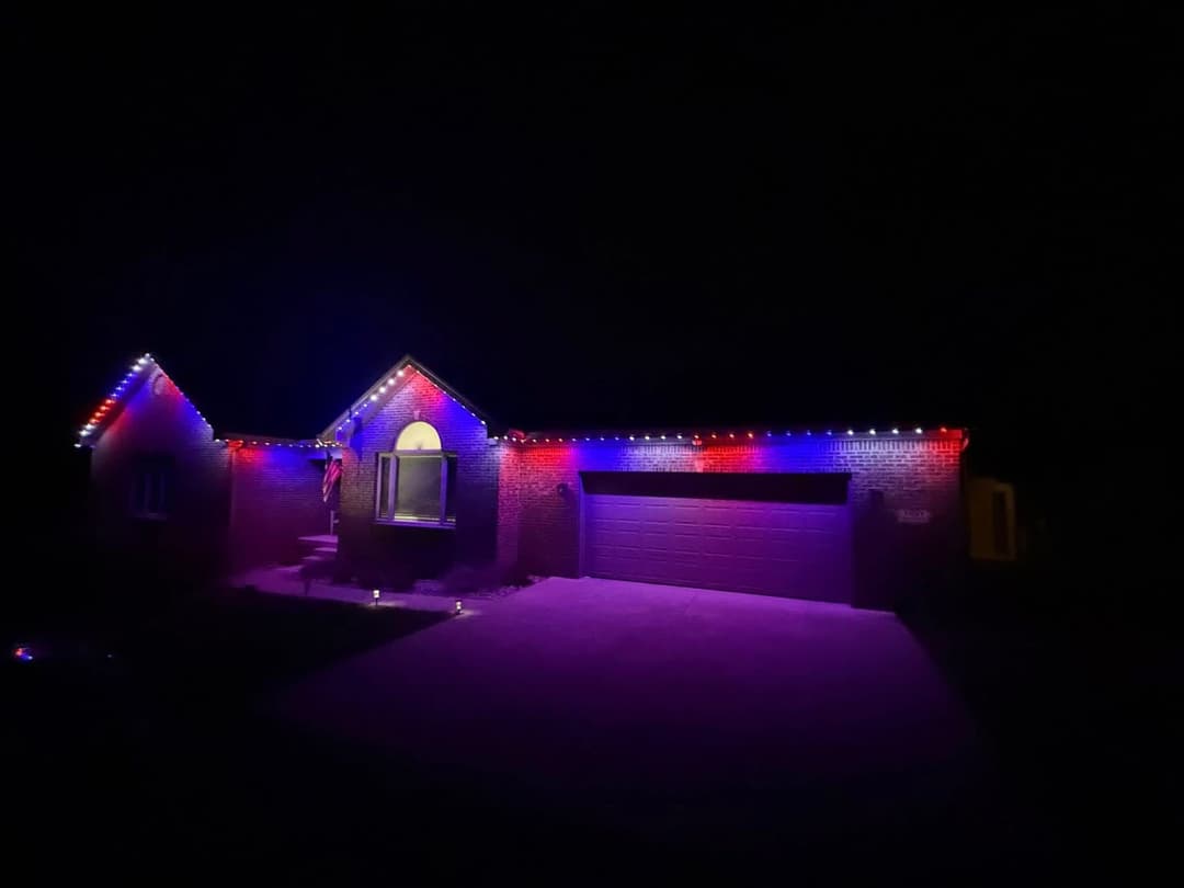 House decorated with colorful red, white, and blue lights for a festive nighttime display.
