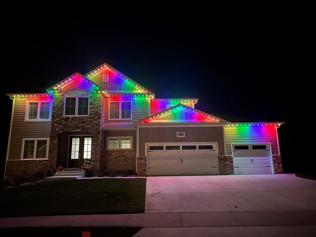 Colorful holiday lights illuminate a modern two-story house at night.
