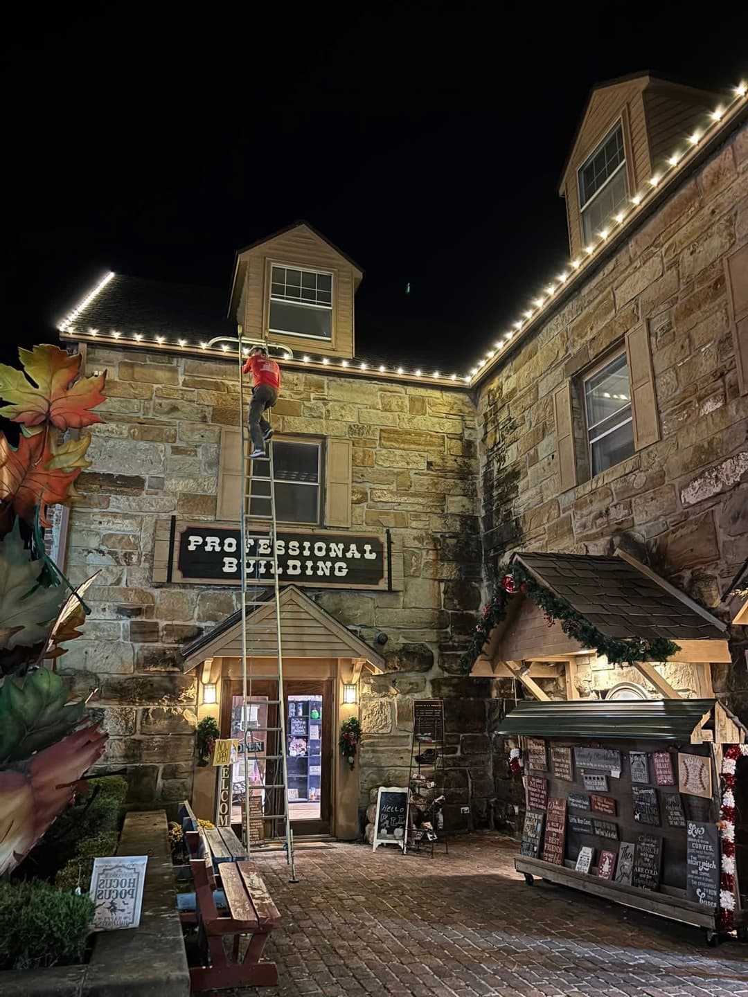 Person on ladder decorating a historic building with holiday lights at night.