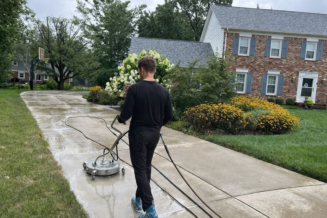 Pressure washing service cleaning a driveway, revealing a spotless surface and vibrant landscaping.