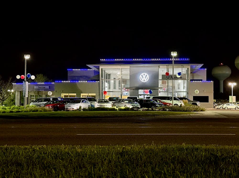 Volkswagen dealership illuminated at night with cars on display and festive decorations.